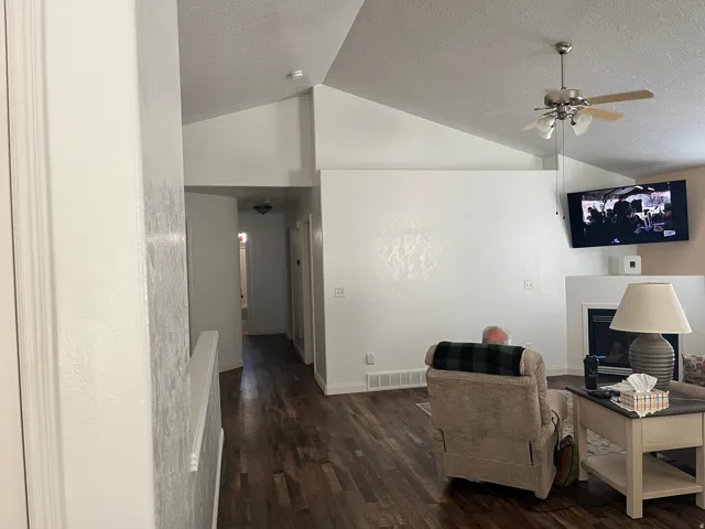Vaulted ceilings, wood-finish flooring, ceiling fan, and a fireplace with a white mantel