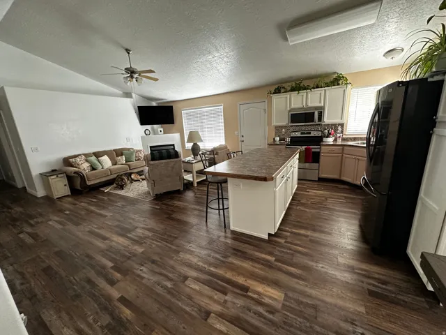 Vaulted ceiling, wood-finish flooring, kitchen island with seating, stainless steel appliances, and a built-in fireplace