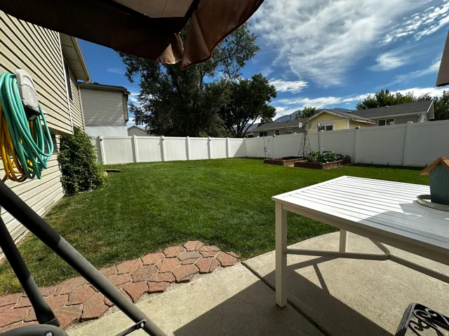 Expansive backyard featuring a green lawn, white privacy fencing, concrete patio, and garden beds