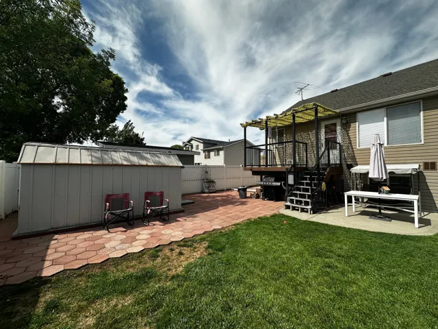 Expansive green lawn with a paver patio and a raised deck featuring a pergola