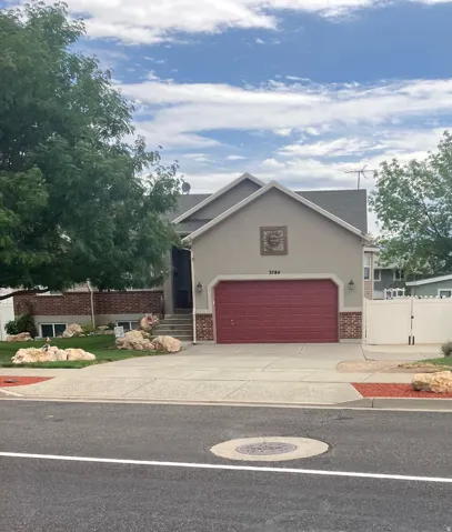 Stucco exterior with brick detailing, attached garage with red door, concrete driveway, and front yard landscaping with decorative rocks