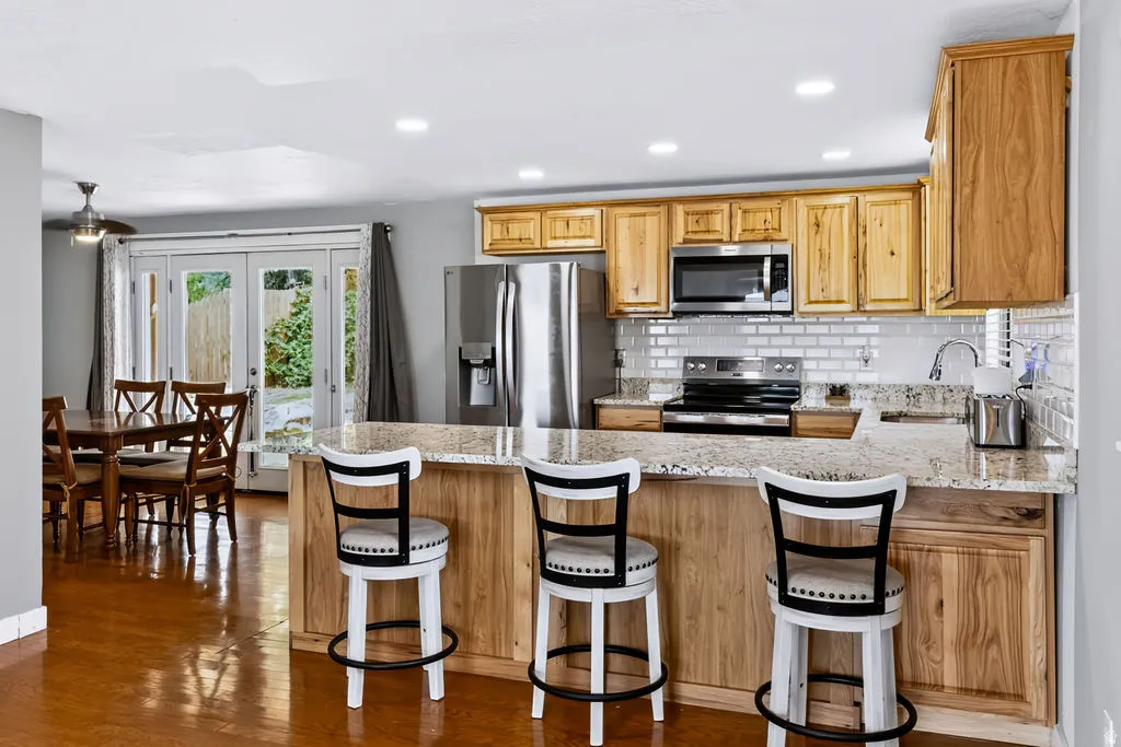 Kitchen featuring wood-finish cabinetry, stainless steel appliances, a light-toned backsplash, a breakfast bar, and recessed lighting