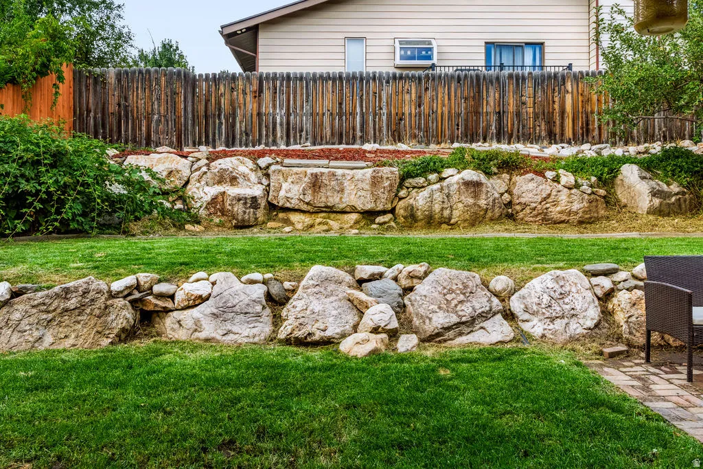 Expansive backyard featuring a manicured lawn, multi-level rock retaining walls, and a wood privacy fence