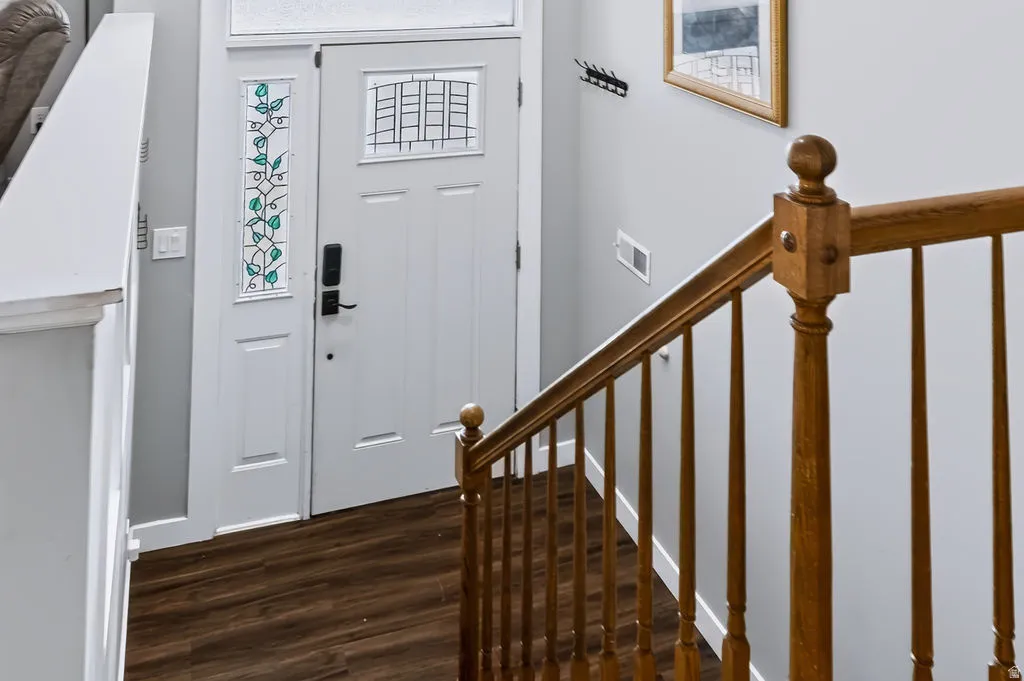 White entry door with decorative glass inserts, sidelight with stained glass, wood-finish flooring, and natural wood staircase with balusters