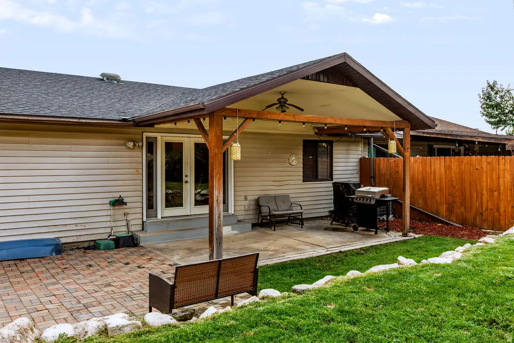 Expansive outdoor living area featuring a covered patio, concrete and brick paver surfaces, and a timber-framed overhang with a ceiling fan