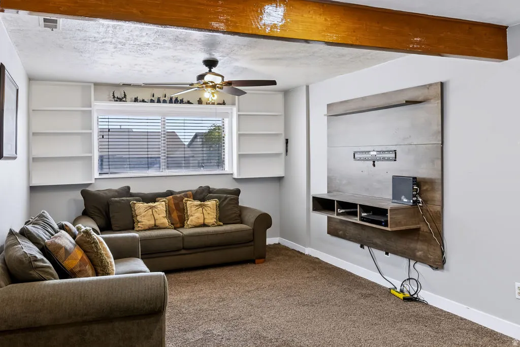 Exposed wooden beam, built-in shelving, window with blinds, ceiling fan with light fixture, and mounted media console