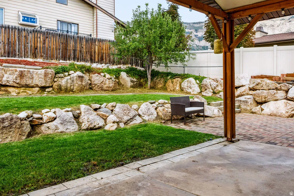 Patio with concrete and paver sections, wood pergola support, lush lawn, and natural rock retaining walls