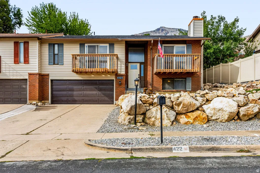 Brick and siding exterior featuring two integral garages, a raised wood deck, and a terraced rock landscape