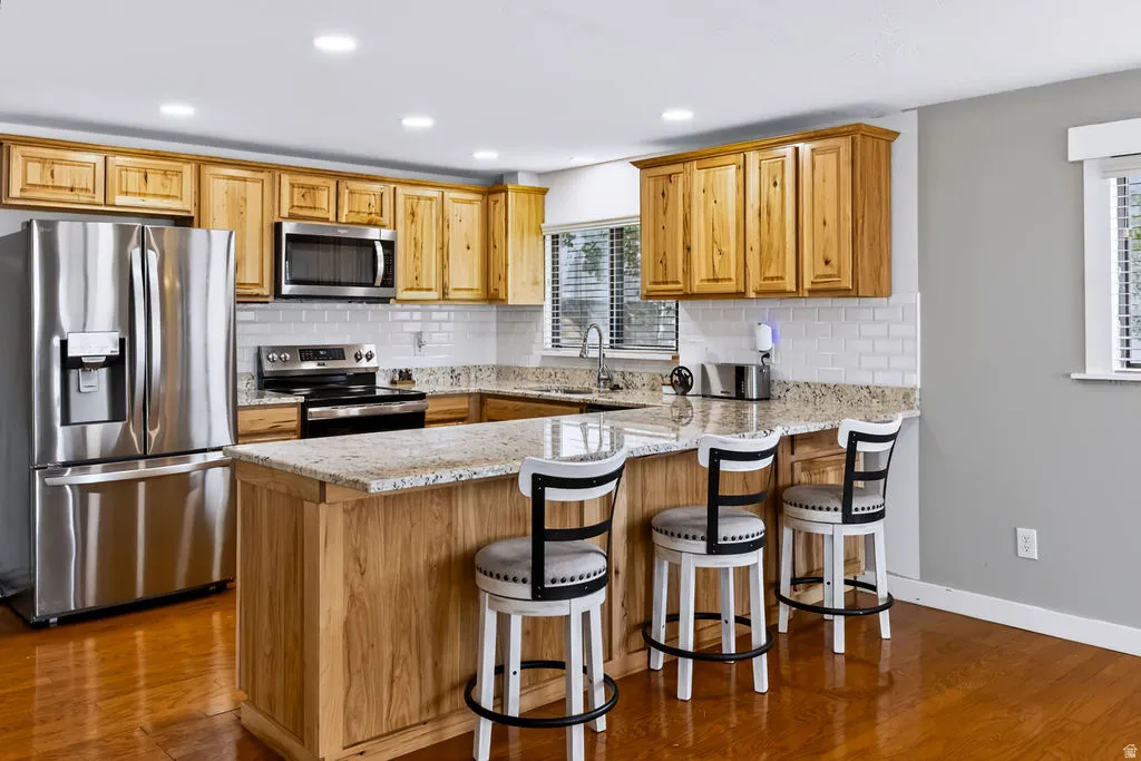 Kitchen featuring wood-finish cabinetry, stainless steel appliances, a center island with counter seating, light-toned countertops, and a subway tile backsplash