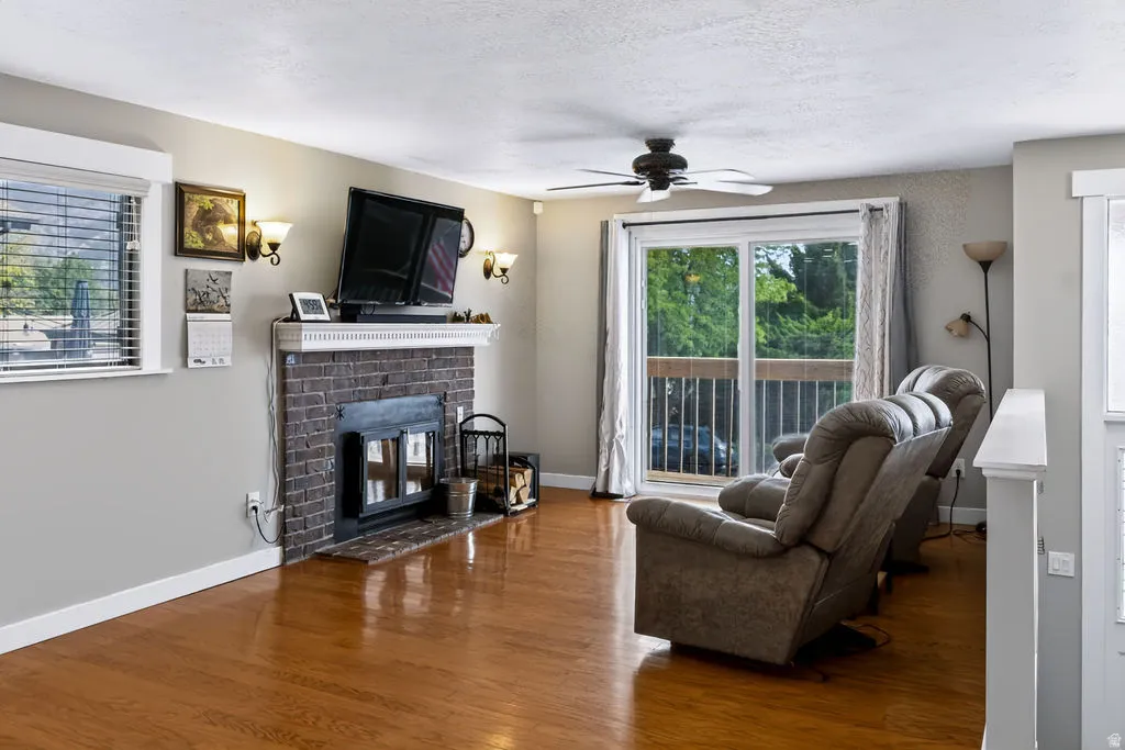 Hardwood flooring, a brick-front fireplace, a ceiling fan, and sliding glass door access to an outdoor area
