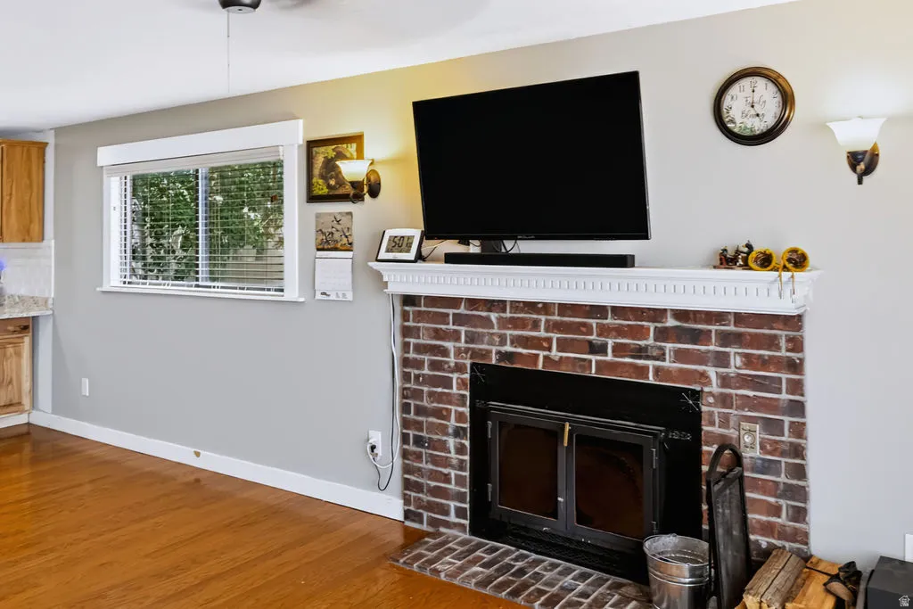 Brick fireplace with an ornate white mantel, wood-finish flooring, and a single window with blinds