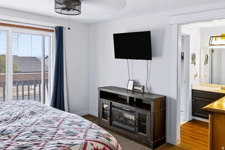 Sliding glass door, ceiling-mounted light fixture, wall-mounted media console with electric fireplace, wood-finish flooring in adjoining space, and a single vanity with an integrated sink