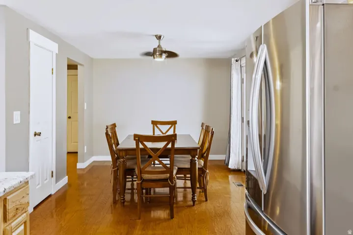 Wood-finish flooring throughout, stainless steel refrigerator, white interior doors with brass hardware, and a ceiling fan with integrated lighting