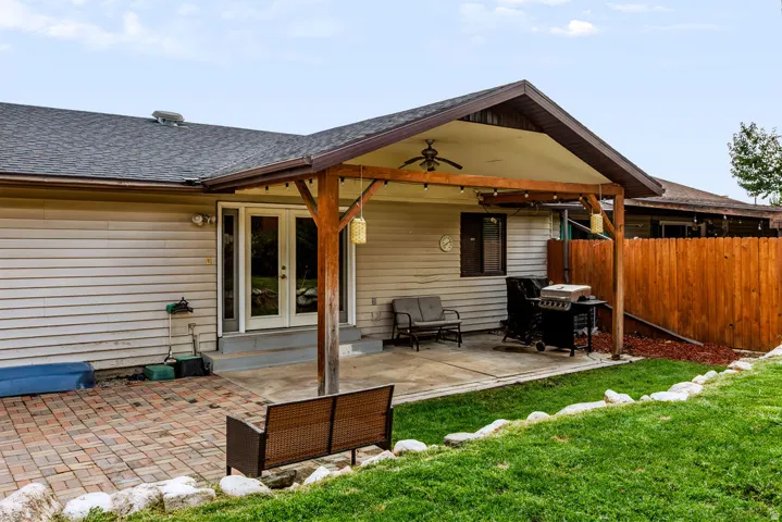 Expansive outdoor living area featuring a covered patio, concrete and brick paver surfaces, and a timber-framed overhang with a ceiling fan