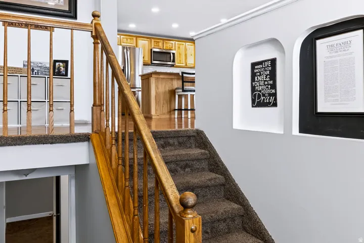 Carpeted staircase with wood banister and railings, recessed wall niches, crown molding, and recessed lighting