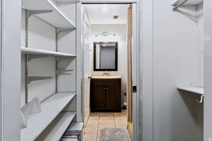 Tile flooring, wood-finish vanity with countertop, framed mirror, and wall-mounted light fixture
