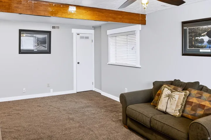 Recessed window with white blinds, neutral wall paint, white trim, exposed wood beam, ceiling fan with light fixture