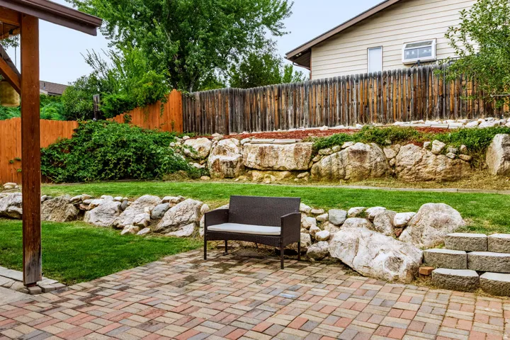 Paver patio with a wood support column, a terraced lawn, natural rock retaining walls, and a wood fence