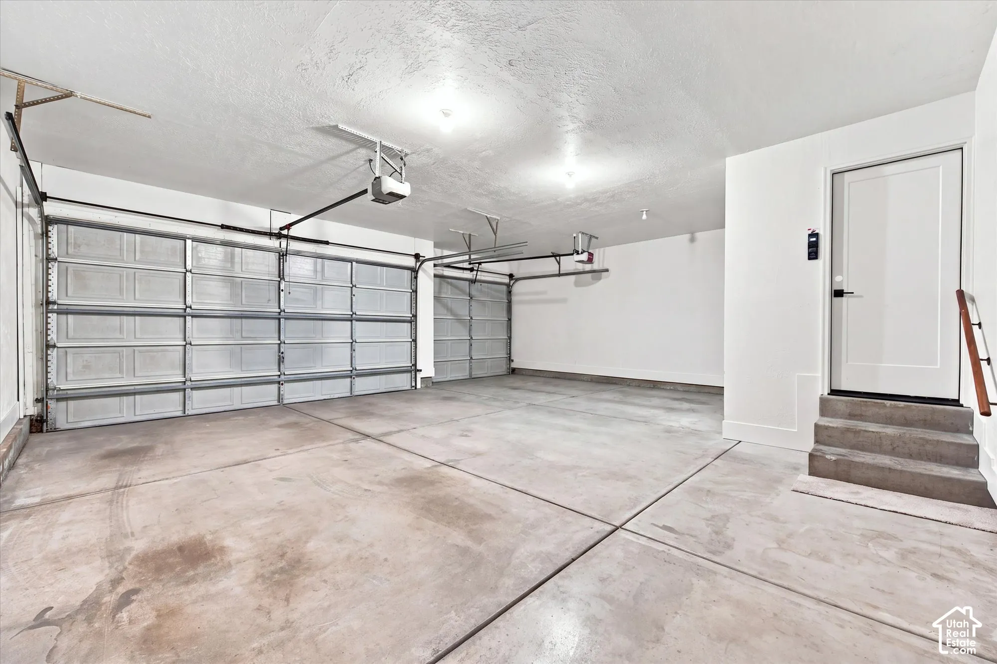 Two automatic garage doors, exposed ceiling joists, concrete flooring, interior access door, and three concrete steps