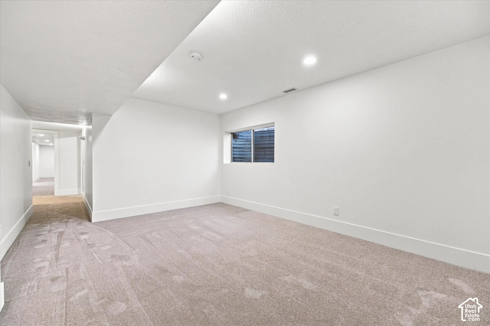 Recessed lighting, window with horizontal blinds, neutral-toned carpeting, white walls, and a hallway