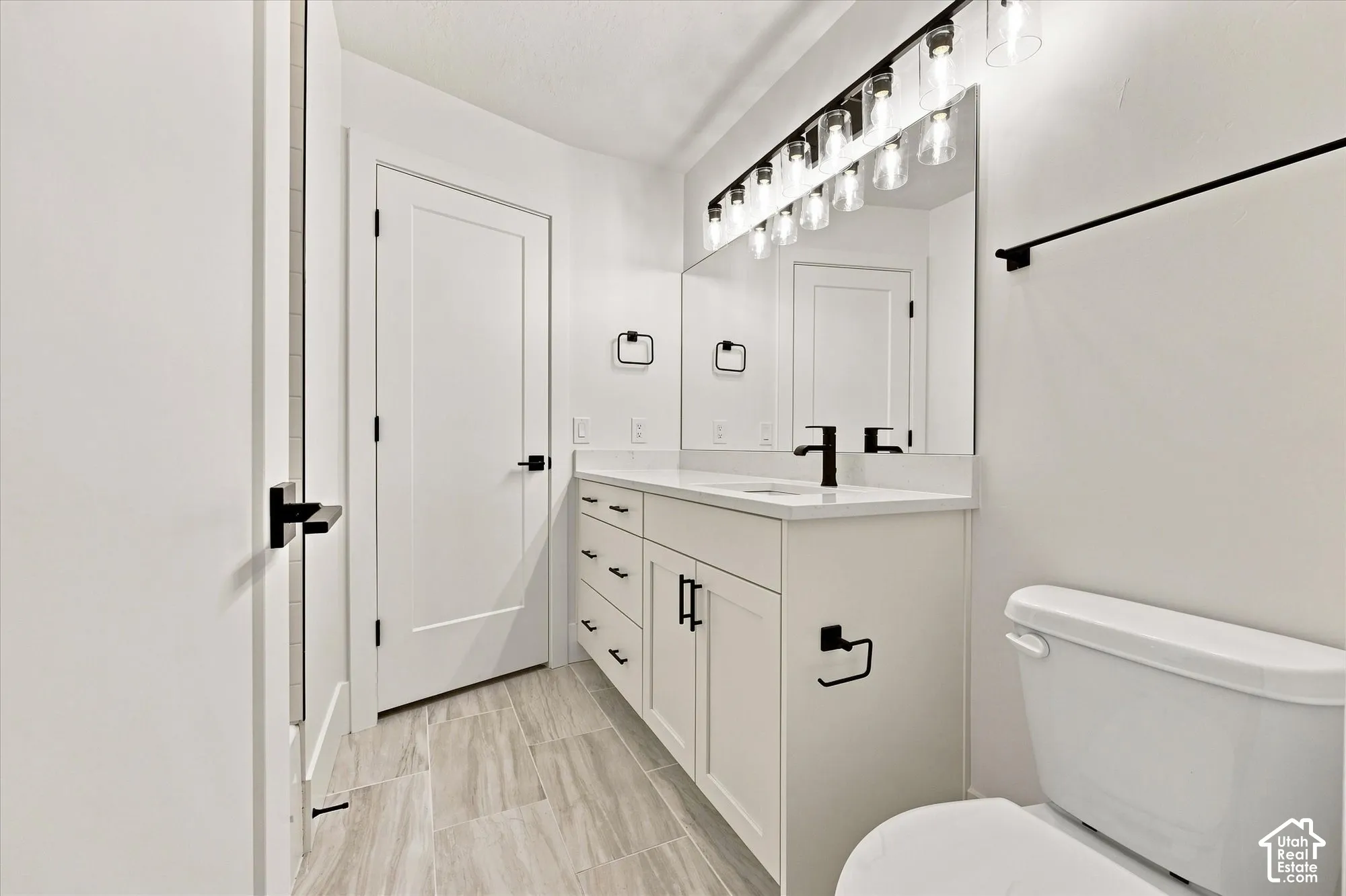 Modern bathroom featuring a white vanity with integrated sink, matte black hardware, a large mirror, and tiled flooring