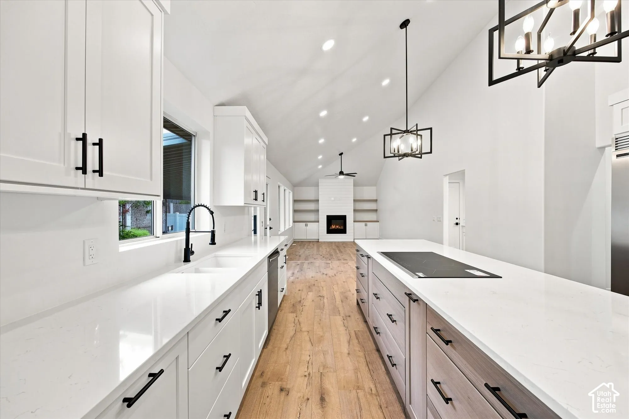 Vaulted ceiling, recessed lighting, wood-finish flooring, white cabinetry with matte black hardware, and integrated cooktop on island