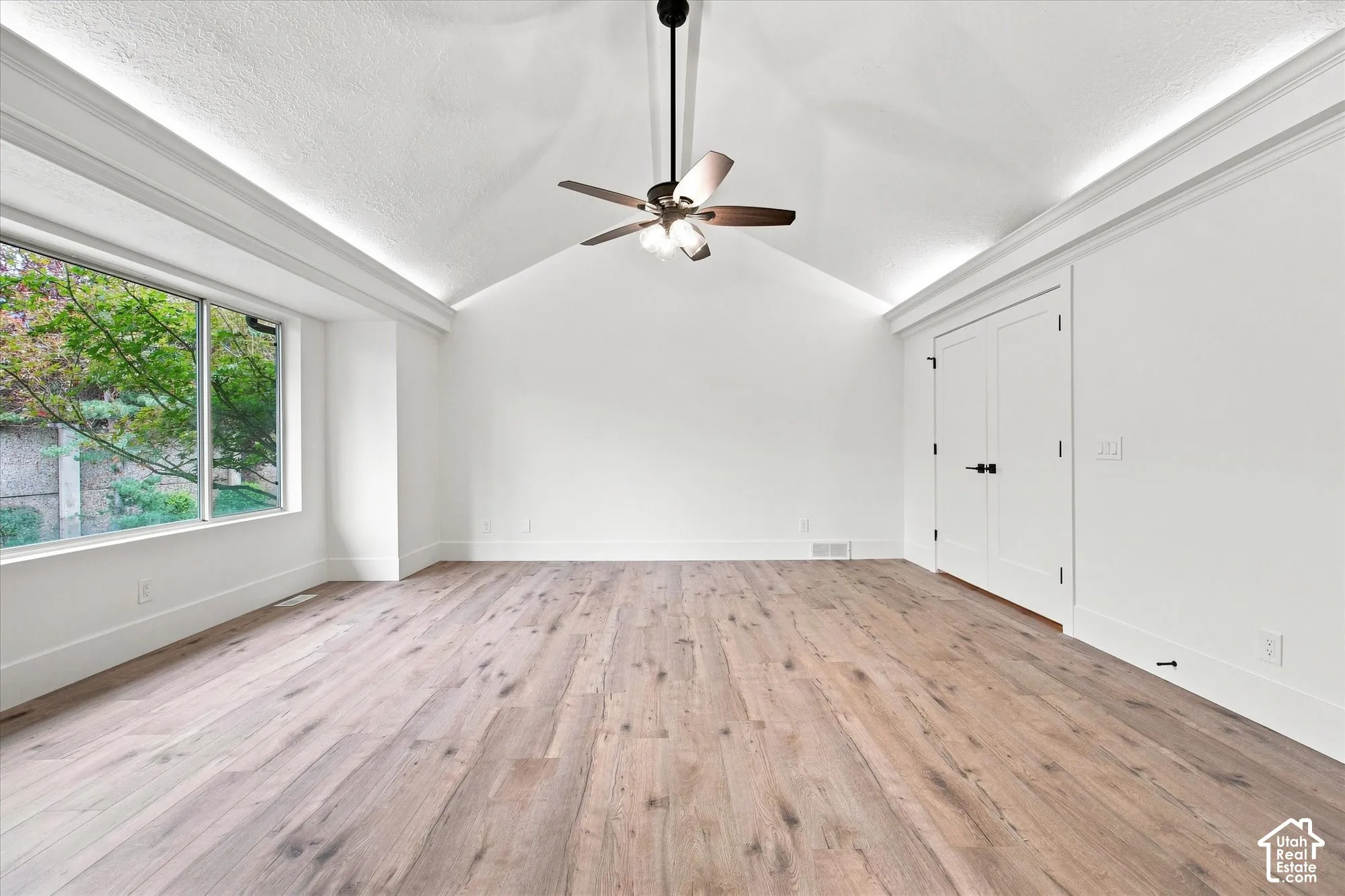 Vaulted ceiling, wood-finish flooring, ceiling fan, large window, and double doors