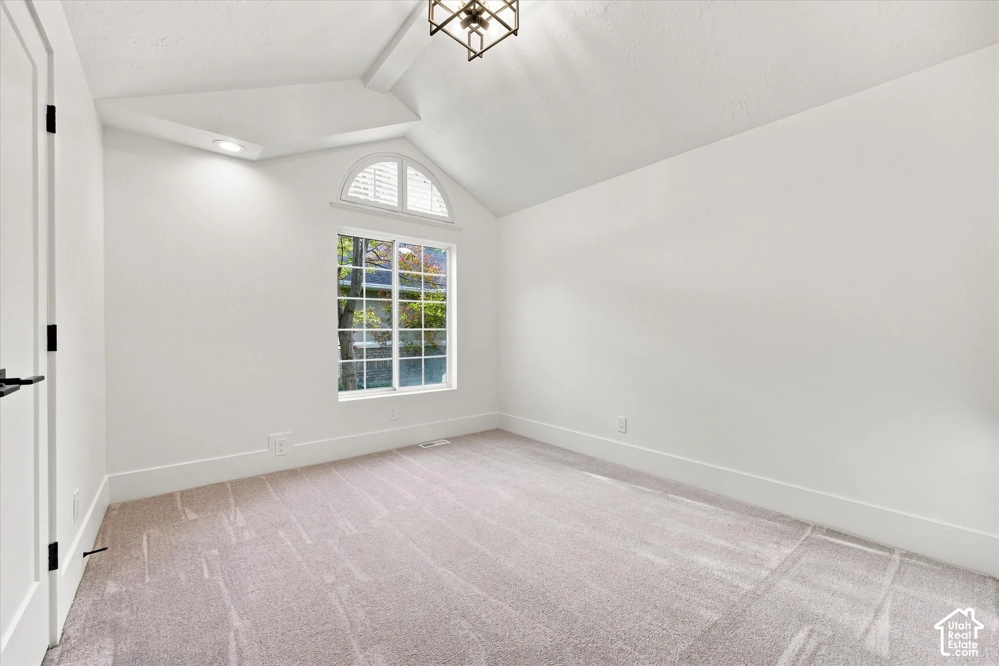 Vaulted ceiling with a decorative light fixture, arched window with white blinds, recessed lighting, and soft gray carpeting