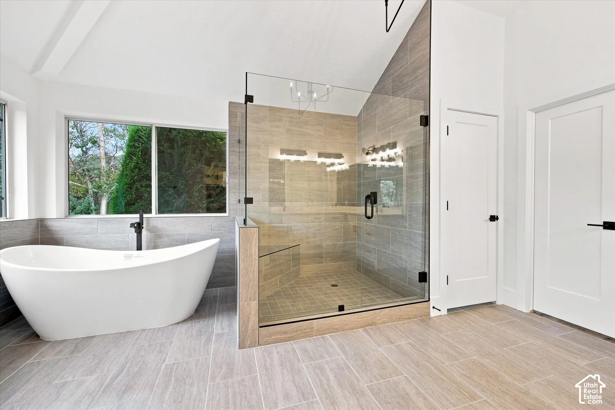 Freestanding bathtub with a floor-mounted faucet, glass-enclosed shower, tiled shower walls, and broad plank-style flooring