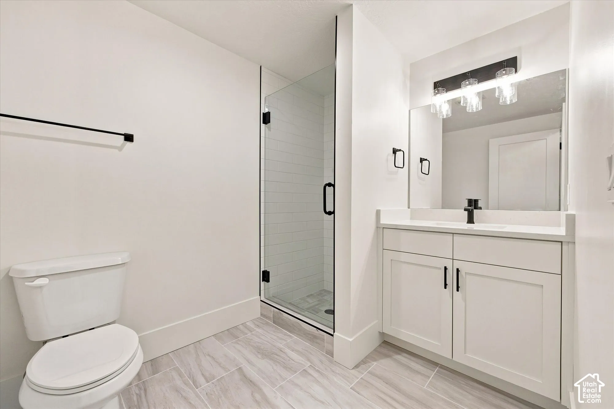 Full bathroom featuring a glass-enclosed shower, white vanity with stone countertop, dark-finish fixtures, and light-toned tile flooring