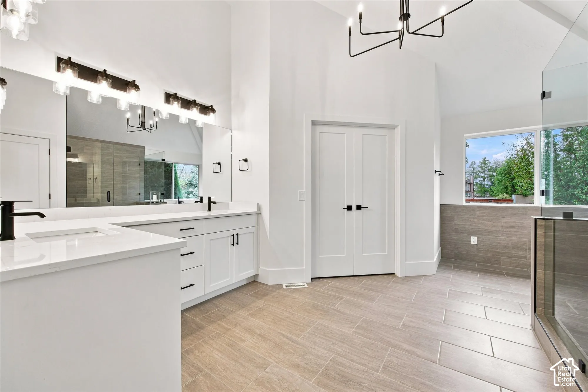 Vaulted ceiling, dual vanity with undermount sinks, quartz countertops, modern black fixtures, and a glass-enclosed shower