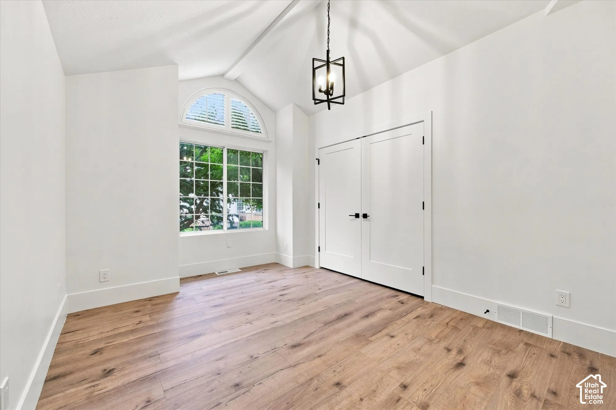 Vaulted ceiling with an exposed beam, wood-finish flooring, arched transom window, white plantation shutters, and a modern chandelier