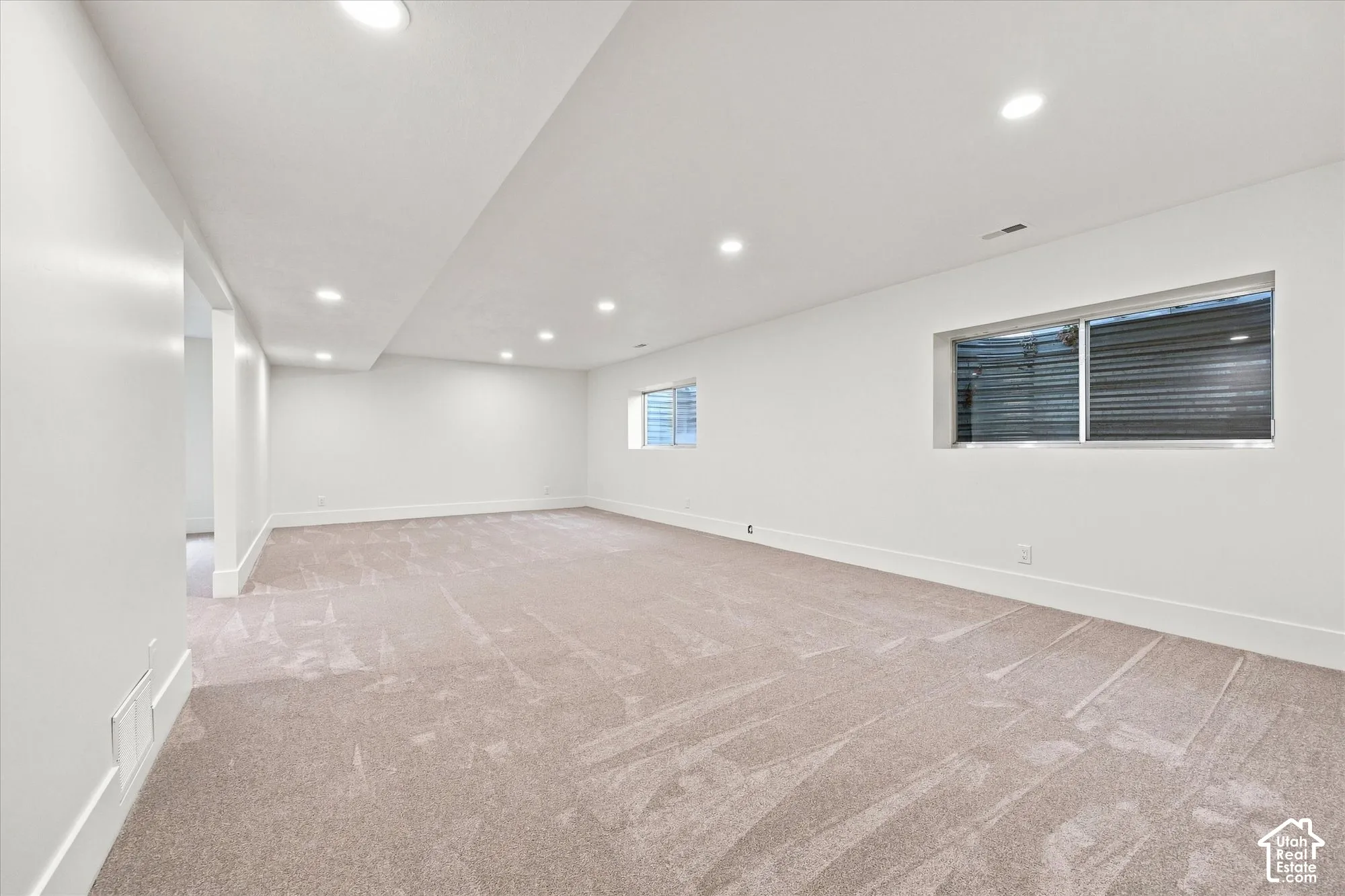 Expansive carpeted area with recessed lighting, multiple windows, and crisp white walls