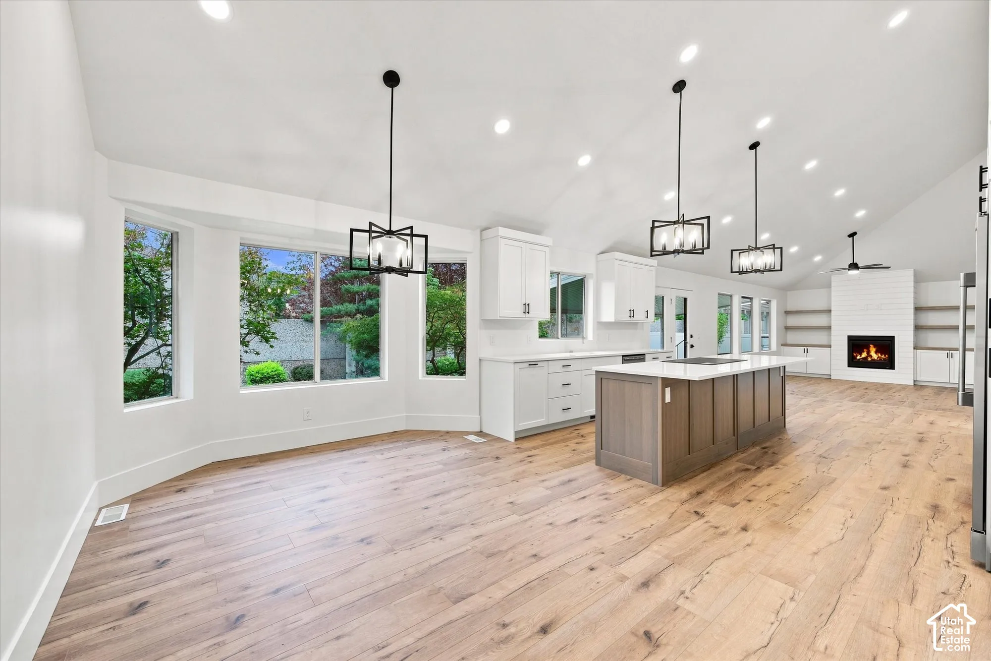 Vaulted ceilings, wood-finish flooring, a kitchen island with seating, a fireplace with a shiplap surround, and recessed lighting