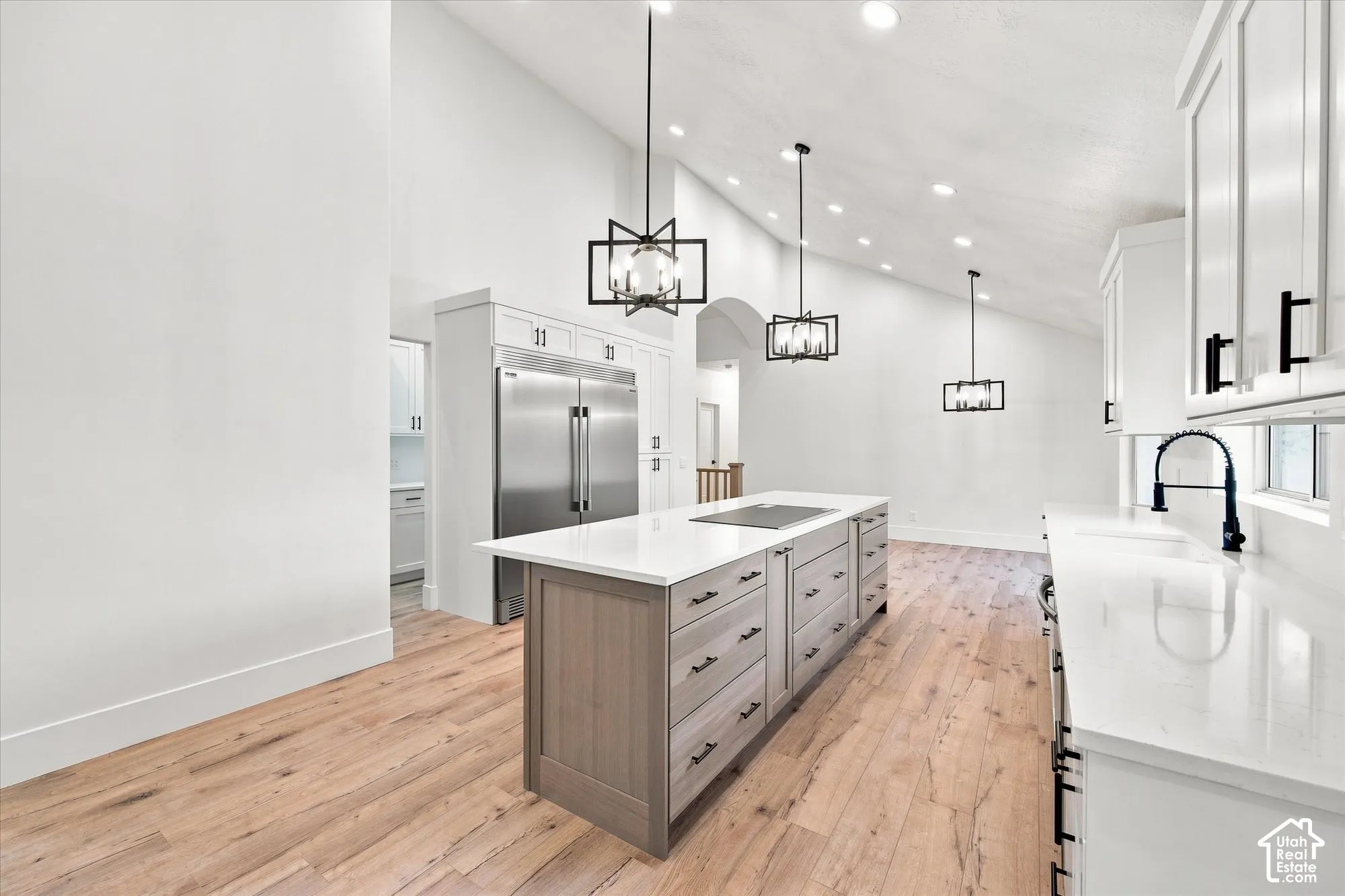 Vaulted ceiling, recessed lighting, wood-finish flooring, central island with integrated cooktop, and stainless steel refrigerator