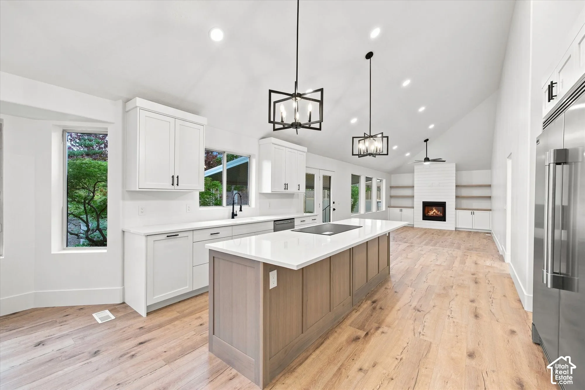 Vaulted ceilings with recessed lighting, wood-finish flooring, kitchen island with built-in cooktop, white cabinetry, and a fireplace with shiplap surround