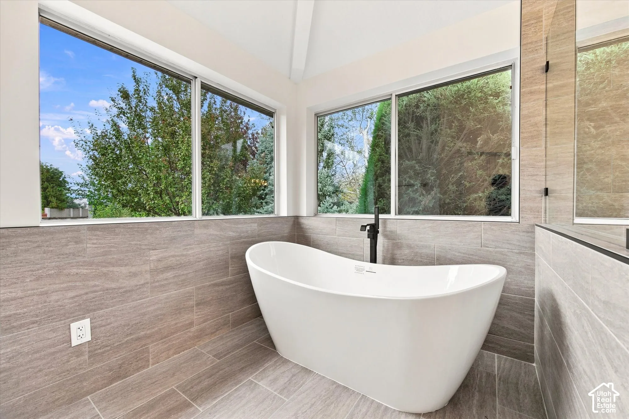Freestanding bathtub with a floor-mounted matte black faucet, surrounded by large format tile flooring and wainscoting