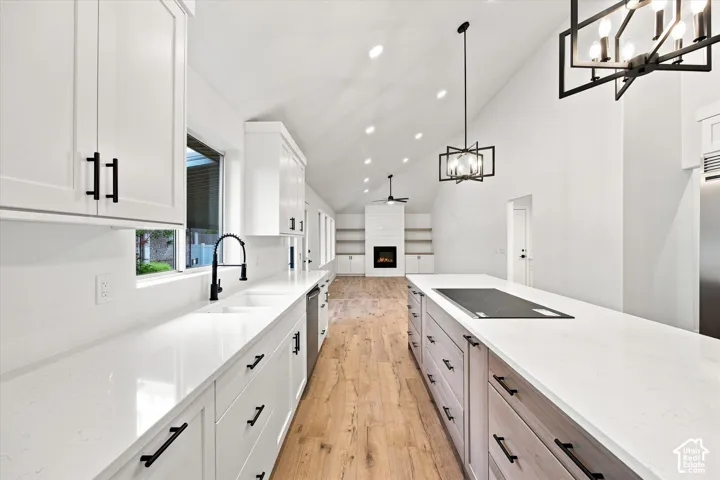 Vaulted ceiling, recessed lighting, wood-finish flooring, white cabinetry with matte black hardware, and integrated cooktop on island