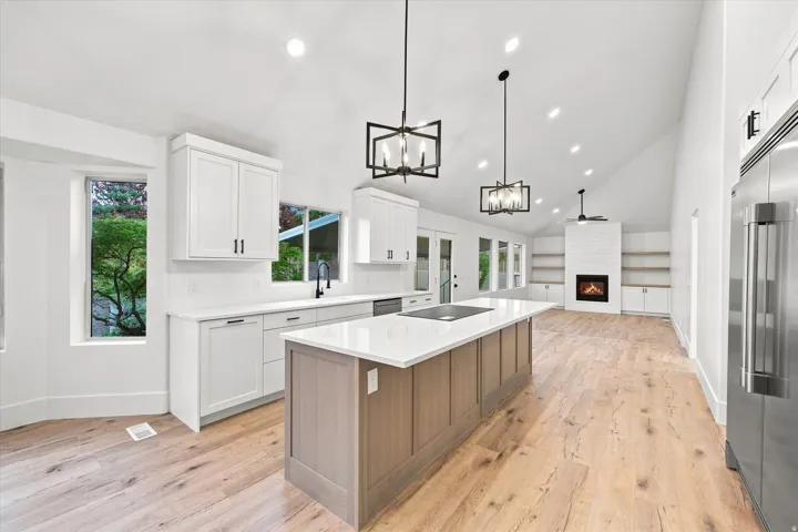 Vaulted ceilings with recessed lighting, wood-finish flooring, kitchen island with built-in cooktop, white cabinetry, and a fireplace with shiplap surround