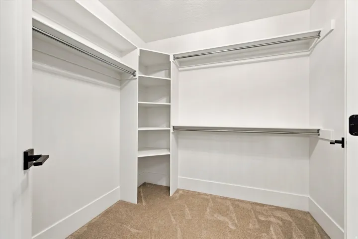 Built-in shelving, multiple hanging rods, and neutral carpet flooring