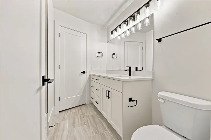 Modern bathroom featuring a white vanity with integrated sink, matte black hardware, a large mirror, and tiled flooring