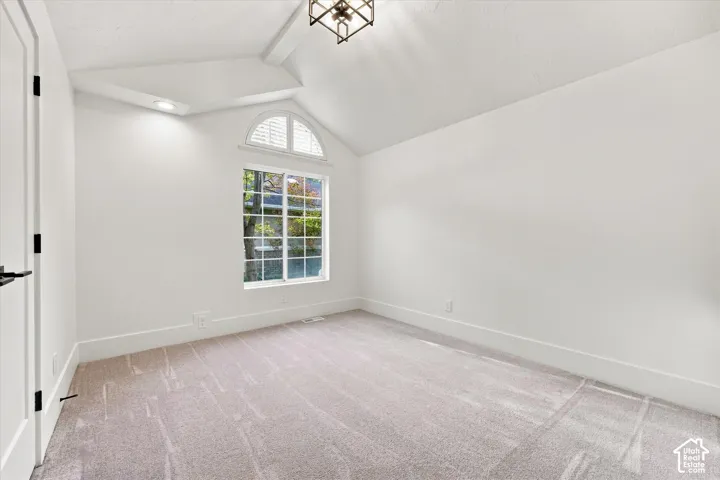 Vaulted ceiling with a decorative light fixture, arched window with white blinds, recessed lighting, and soft gray carpeting