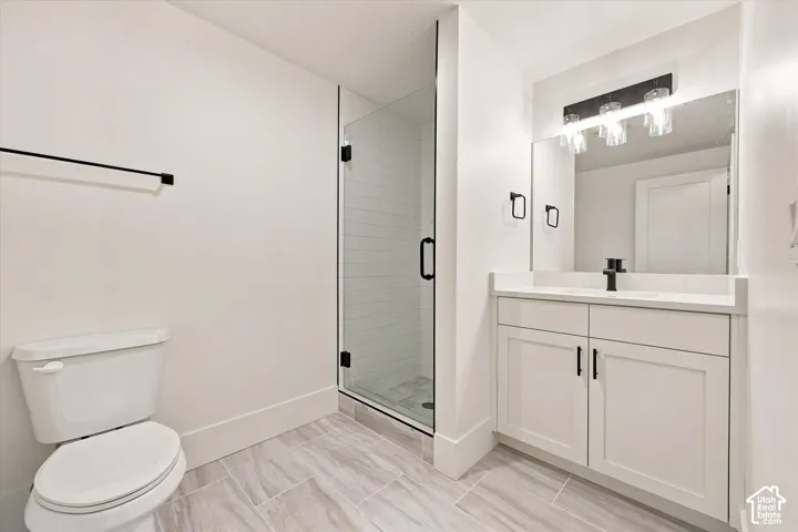 Full bathroom featuring a glass-enclosed shower, white vanity with stone countertop, dark-finish fixtures, and light-toned tile flooring