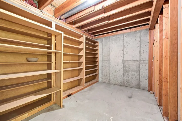 Extensive built-in shelving, exposed wood ceiling joists, concrete flooring, and concrete foundation walls