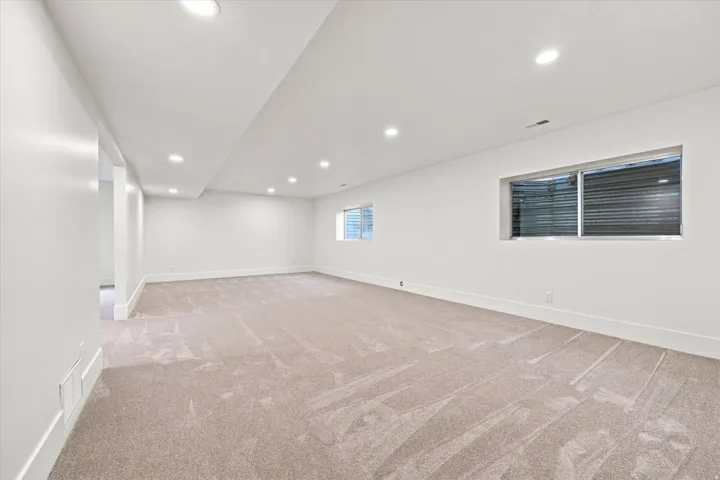 Expansive carpeted area with recessed lighting, multiple windows, and crisp white walls