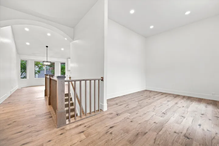 Recessed lighting, wood-finish flooring, staircase with wood railing, arched ceiling detail, and large window openings