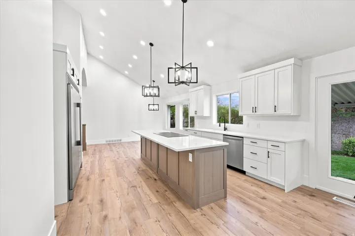 Expansive kitchen featuring a large central island with integrated cooktop, white shaker cabinetry, stainless steel appliances, and wood-finish flooring