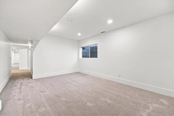 Recessed lighting, window with horizontal blinds, neutral-toned carpeting, white walls, and a hallway