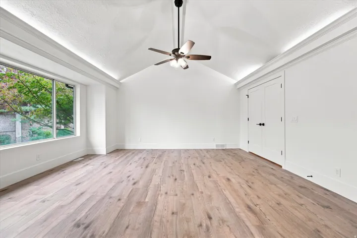 Vaulted ceiling, wood-finish flooring, ceiling fan, large window, and double doors