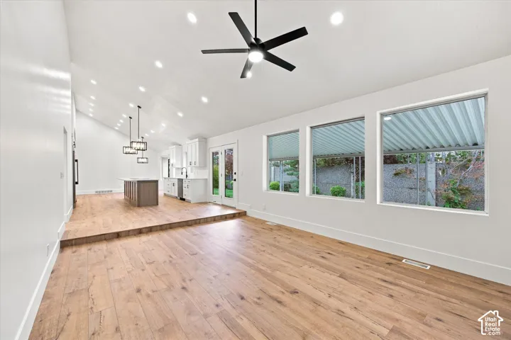 Vaulted ceiling with recessed lighting and a ceiling fan, wood-finish flooring, white walls, and multiple windows